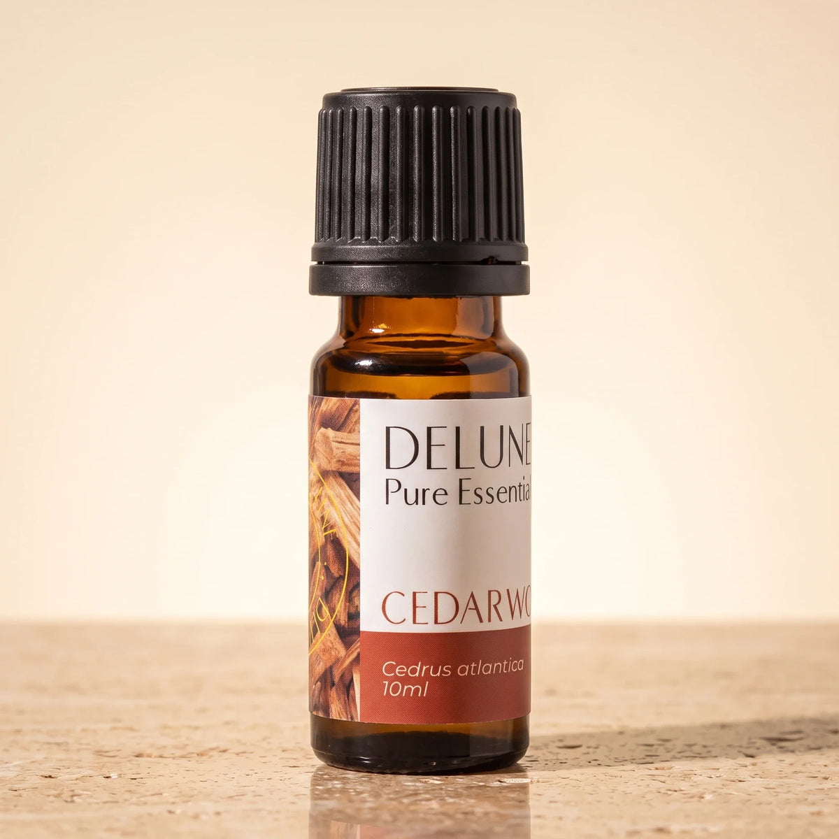 Delune Cedarwood Pure Essential Oil, 10ml amber glass bottle on warm travertine stone