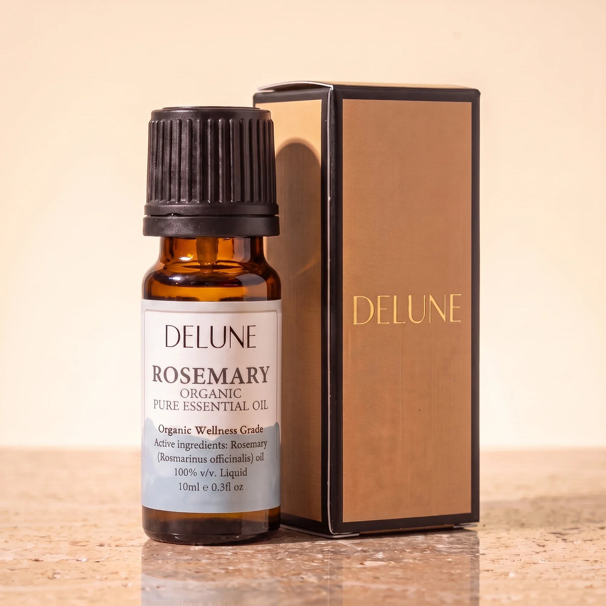 Delune Rosemary Organic Wellness Grade Essential Oil, 10ml amber glass bottle with its gold-foil Delune gift box on warm travertine stone