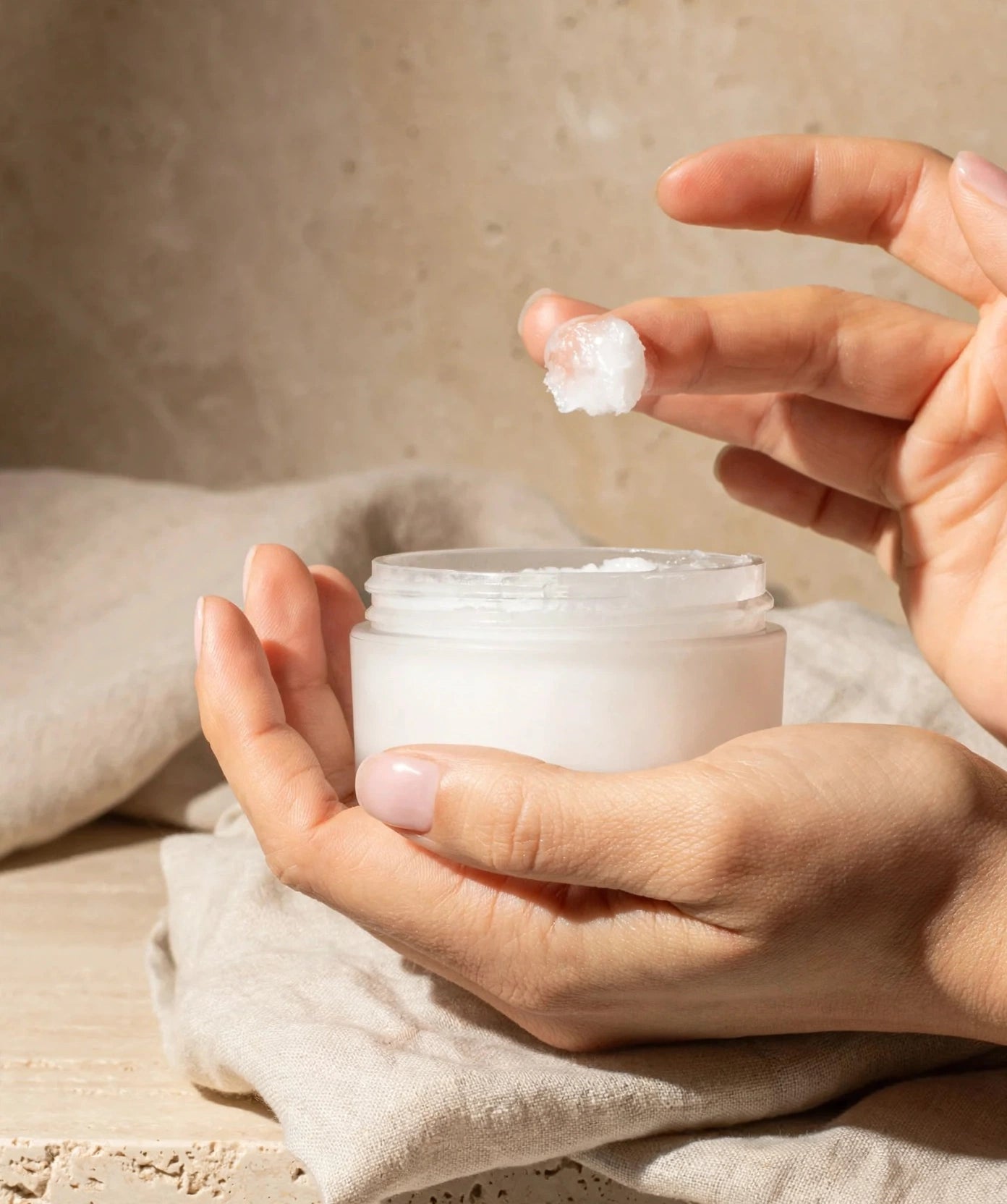 Raw coconut cream cleanser scooped from the jar in soft warm light