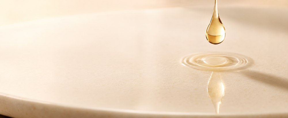 A suspended drop of lightweight facial oil above a pale ceramic surface